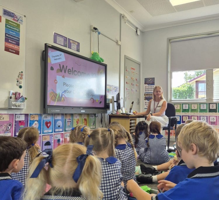 Image of a teacher in her classrooms with students looking at her.
